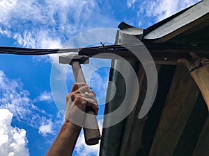 A man hammers nails with a hammer against the blue sky. a gold ring is worn on his right hand. repair work at height. metal hammer