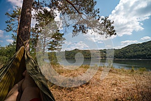 Man in hammock, first person look view, warm summer day, pine tree. river and mountains background. Travel and vacation, tourism