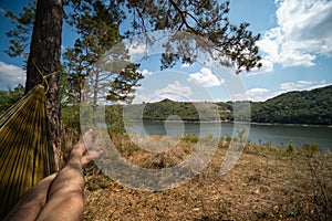 Man in hammock, first person look view, warm summer day, pine tree. river and mountains background. Travel and vacation, tourism