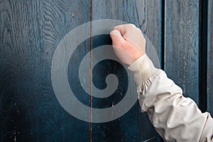 man hand in a beige jacket knocks on a blue wooden door Anybody home