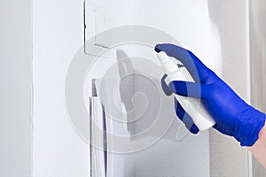 Man hand in blue glove cleaning door phone with sanitizer