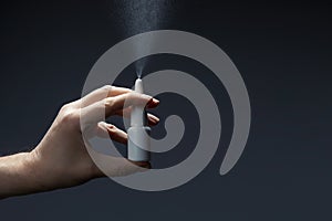 Man hand with a bottle of medication for runny nose during grippe on dark background. Treatment colds via a nasal spray photo