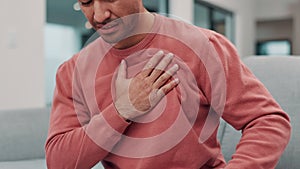 Man, hand and chest pain with injury, heart attack or ache on living room sofa at home. Closeup of male person in panic