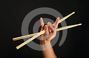 Man hand with crossed drumsticks and devil horns over black