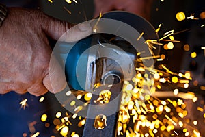 Man hand cuts metal bar using electric grinder with sparks flying around