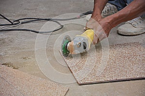 man hand cutting a tile using an angle grinder on the floor