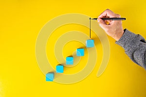 Man hand drawing an upward pointing arrow on top of growing graph made of wooden block