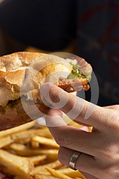 Man hand eating chorizo â€‹â€‹sandwich traditional Argentine food called choripan with French fried in a dish