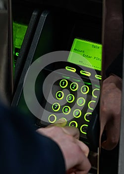 Man hand entering PIN on green illuminated atm machine keypad