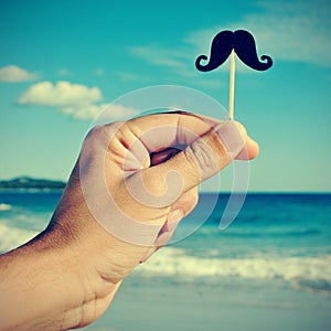 man hand with a fake moustache on the beach, with a filter effect