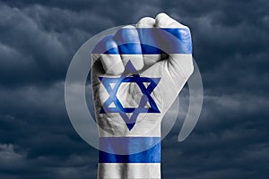 Man hand fist of ISRAEI flag painted. Against the background of dark clouds.