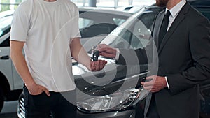 Man hand gives a car keys to male hand in the car dealership close up. Unrecognized auto seller and a man who bought a