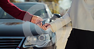 Man hand gives a car keys to woman hand in the car dealership close up. Unrecognized auto seller and a woman who bought