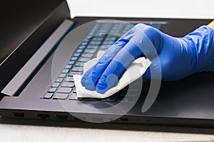Man hand in a glove cleans the laptop keyboard with an antibacterial agent to protect against the epidemic covid-19 disease