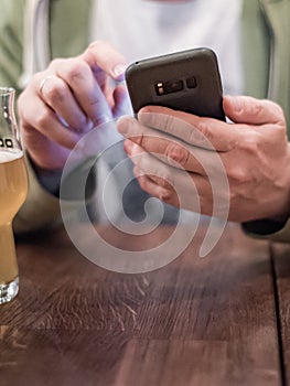 Man hand hold smartphone, drinking beer and reading message at bar or pub