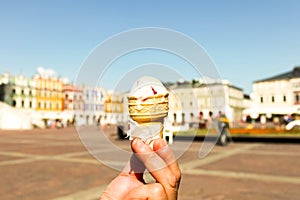 Man hand hold vanilla berry ice cream gelato in a waffle cone on blurred old city background