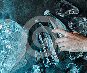 Man hand holding bottle of water in ice. Pieces ice illuminated with blue light. Advertising mineral water in glass bottle, top