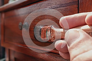 Man hand holding a brush applying varnish paint on a wooden surface. Concept protect  and renovate the wood