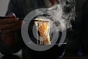 Man hand holding chopsticks of instant noodles in wood bowl with smoke rising in the home, Sodium diet high risk kidney failure,