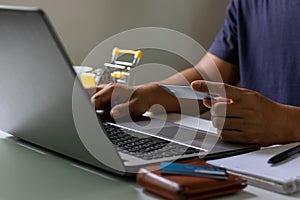 Man hand holding credit card and typing on laptop computer for safe online payment and electronic money transfer security.