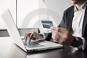 Man hand holding credit card and using laptop computer. Businessman or entrepreneur working at office.