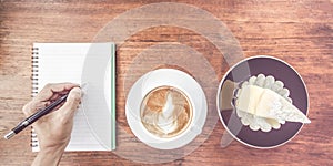 Man, Hand holding cup of coffee,With notebook and pen on wooden table.