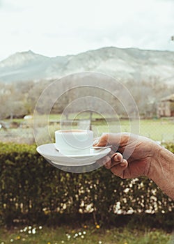 Man hand holding a cup of coffee on a old stone table with mountain landscape
