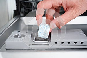 A man hand holding dishwasher detergent tablet. Putting tab into dishwasher, close up. Dishwasher machine full loaded