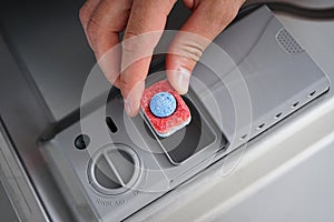 A man hand holding dishwasher detergent tablet. Putting tab into dishwasher, close up.  Dishwasher machine full loaded