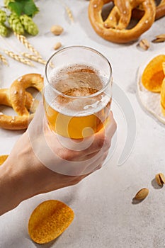 Man hand holding a glass of light beer. Various snacks around