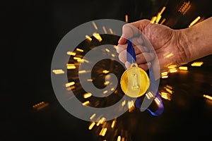 Man hand holding gold medal against black background. Award and victory concept.