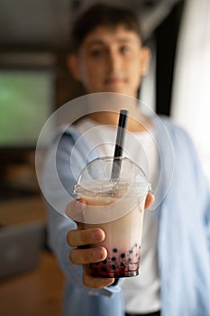 Man hand holding iced milk bubble tea with tapioca pearls and shows it to camera, traditional drink of Taiwan.