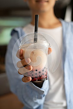 Man hand holding iced milk bubble tea with tapioca pearls and shows it to camera, traditional drink of Taiwan