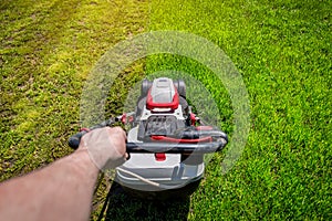 Man hand holding a lawn mower machine to cutting green grass