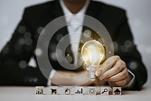 Man hand holding light bulb with Business icon on wood cube and working on desk, Creativity, and innovation are keys to success. C