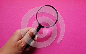 Man hand holding Magnifying glass  on a pinkbackground