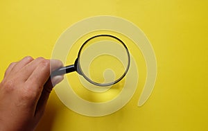 Man Hand holding Magnifying glass  on a yellow backgrou