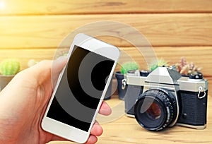 Man hand holding mobile phone blank screen with camera cactus and wood background.