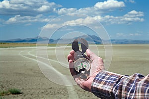 Man hand holding an orientation compass with beautiful desert scenery on the background with copy space for your text