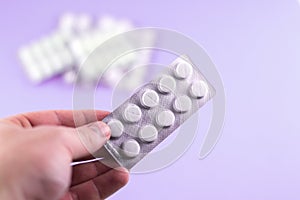 The man hand is holding a pack of white pills packed in blisters with copy space on purple background. Focus on foreground, soft b