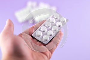 The man hand is holding a pack of white pills packed in blisters with copy space on purple background. Focus on foreground, soft b