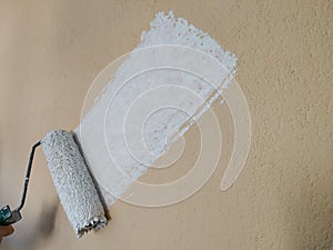 Man hand holding paint roller and painting the wall from orange to white color with visible contrast, while renovating and house