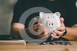 Man hand holding piggy bank on wood table, saving money wealth and financial concept, Business, finance, investment
