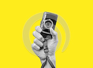 Man hand holding point and shoot camera. Black and white image on yellow background. Practical and compact digital
