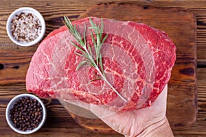 Man Hand Holding a Raw Fresh Steak with Rosemary above a Cups with Herbs