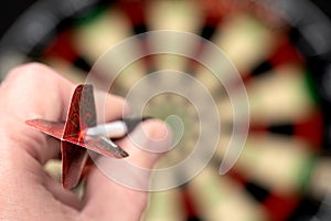 man hand holding red dart at middle of dartboard, which is blurred background. Hitting target. Darts competitions