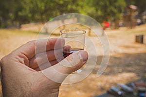 Man hand holding a shot glass with red wine at a social meeting