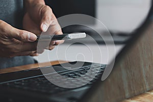 Man hand holding smart phone, and Businessman`s hand using a smartphone for SMS messages with a laptop computer in an office.