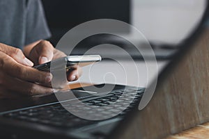 Man hand holding smart phone, and Businessman`s hand using a smartphone for SMS messages with a laptop computer in an office.