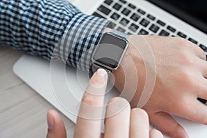 Man hand holding a Watch on the background of laptop